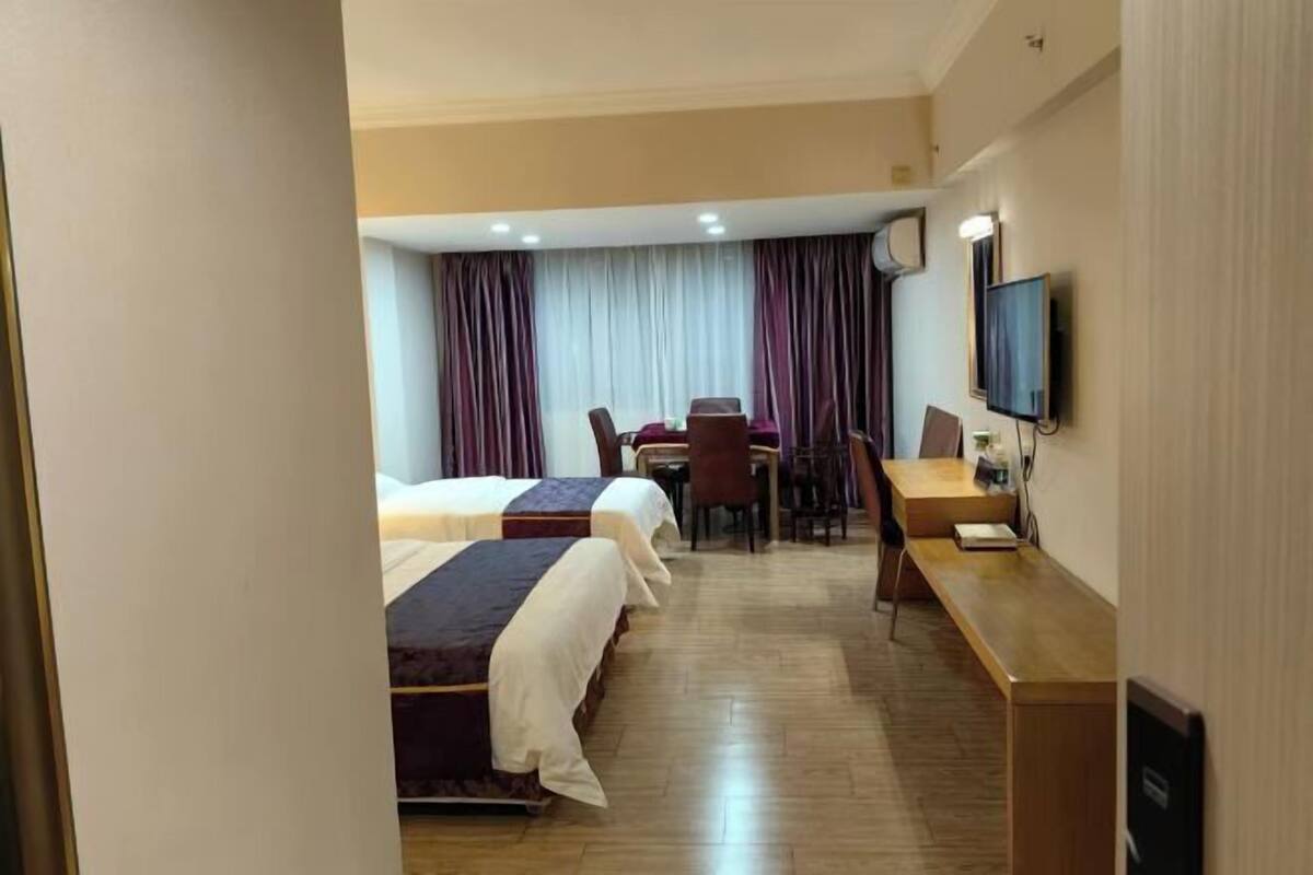 A hotel room with two beds, a desk, a chair, and a television.