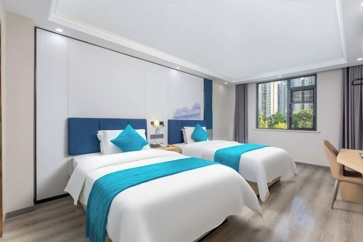 A hotel room with two beds, a desk, and a window with a view of buildings.