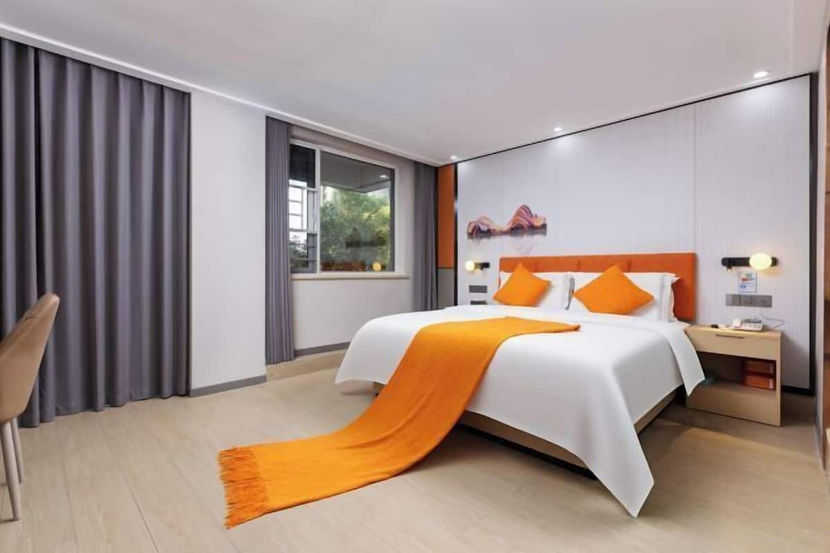 A modern hotel room with a bed, a nightstand, a chair, and a window with curtains.