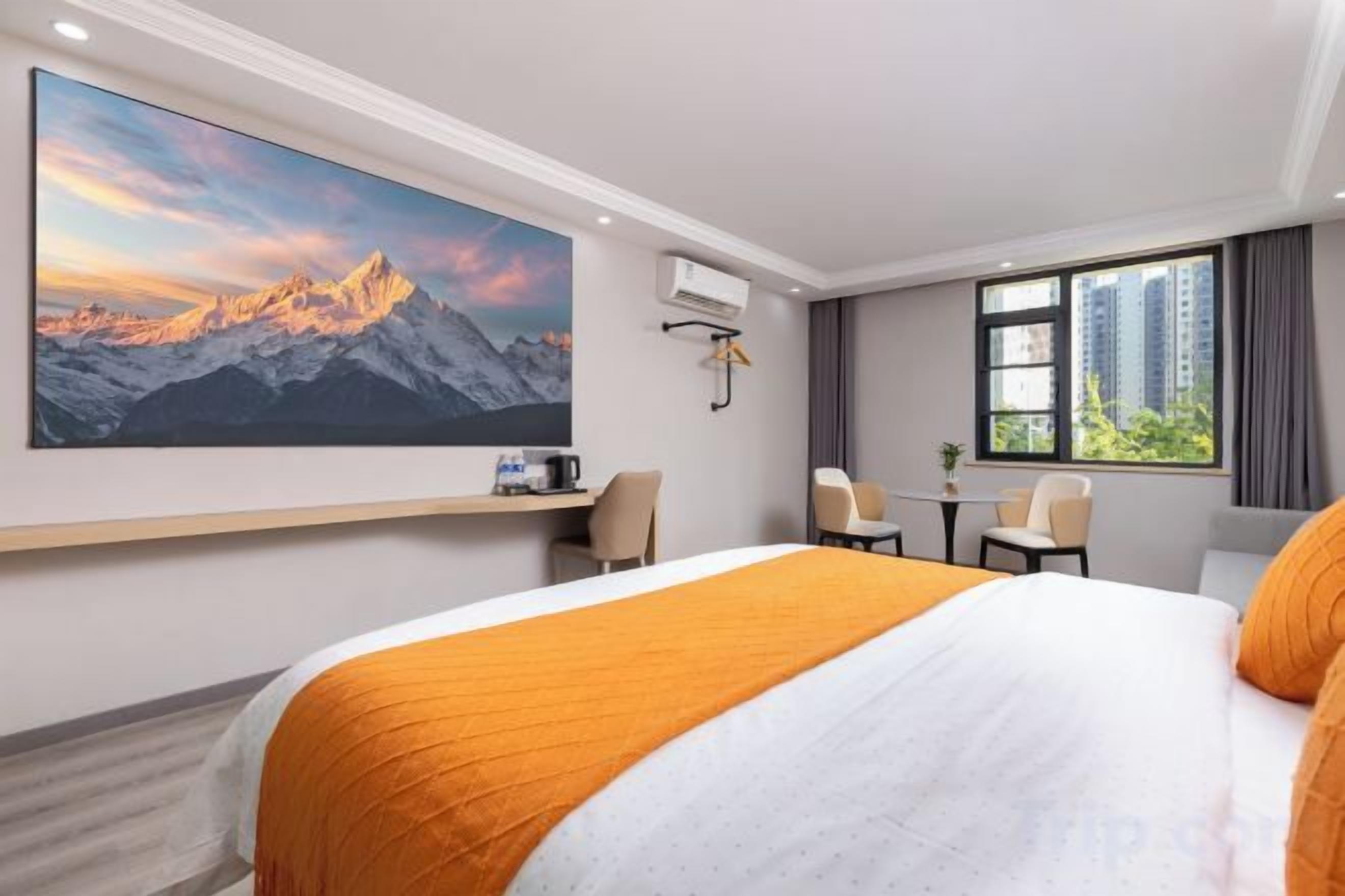 A hotel room with a large bed, a desk, a chair, and a window with a city view.