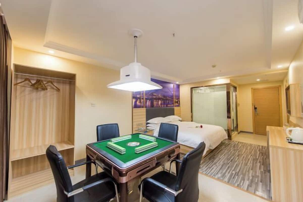A hotel room with a green pool table, a bed, a desk with a lamp, and a wardrobe.