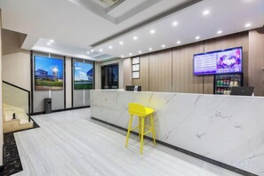 A hotel reception area with a marble counter, a yellow chair, and a TV screen displaying information. - City Youpin Hotel (Wuhan Zuoling New City) (Wuhan)
