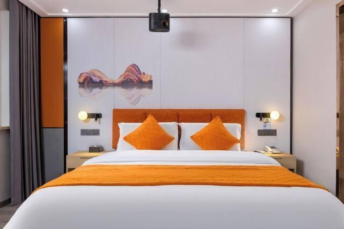 A hotel room with a large bed, two bedside tables, a wall-mounted projector, and a painting.