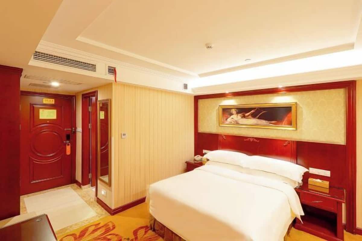 A hotel room with a bed, bedside table, and a painting on the wall.