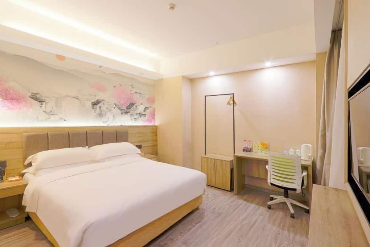 A hotel room with a bed, desk, chair, and a large abstract painting on the wall.