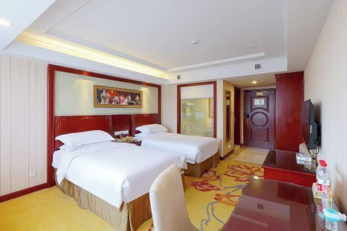 A hotel room with two beds, a desk, a television, and a painting on the wall.