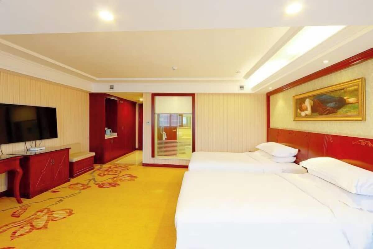 A hotel room with a bed, a TV, a desk, and a painting on the wall.
