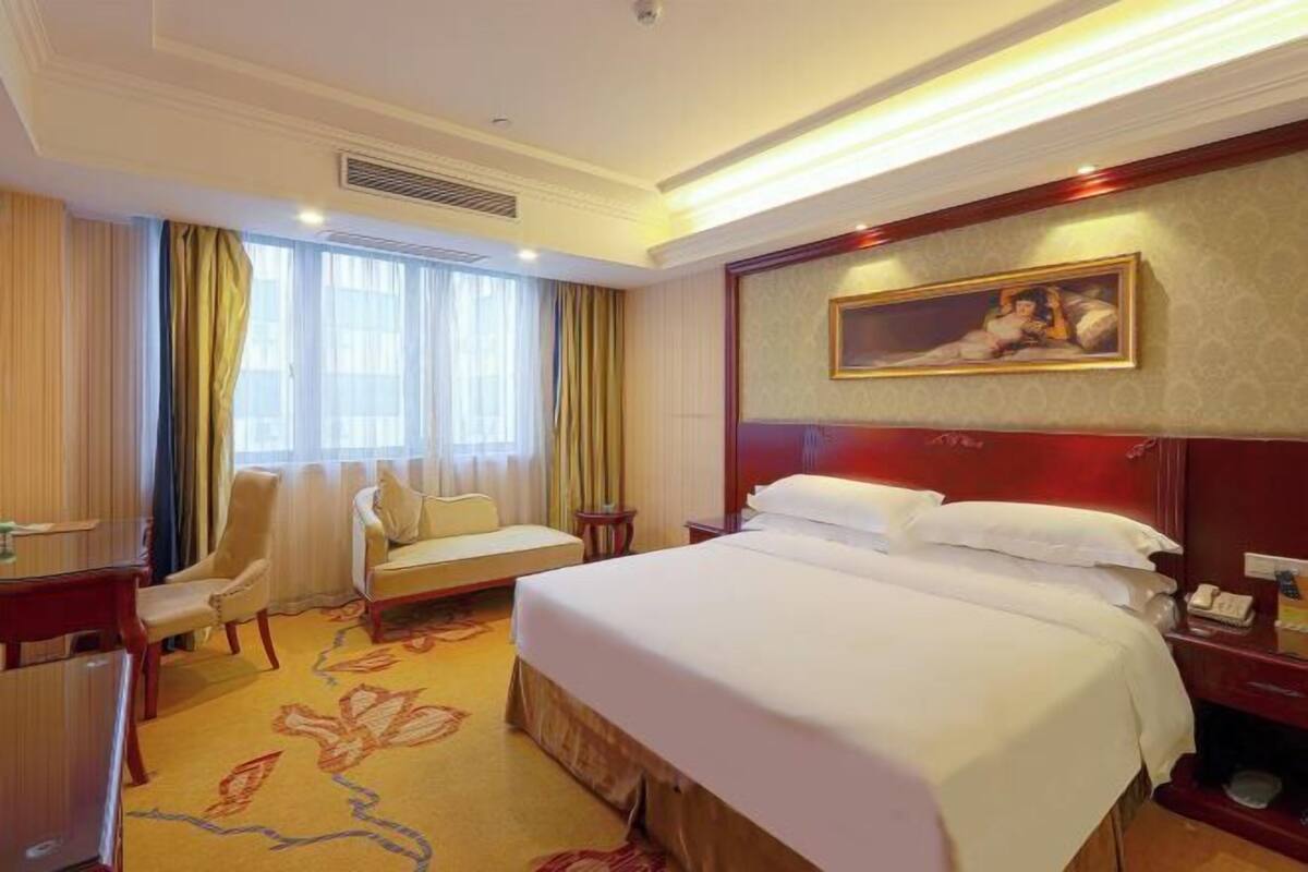 A hotel room with a large bed, a desk, a chair, and a sofa.