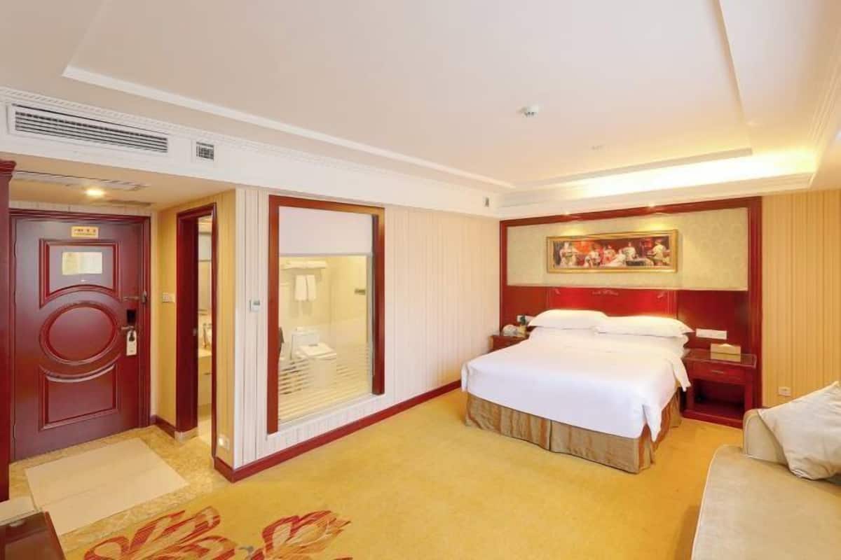 A hotel room with a large bed, a bedside table, a mirror, and a door.