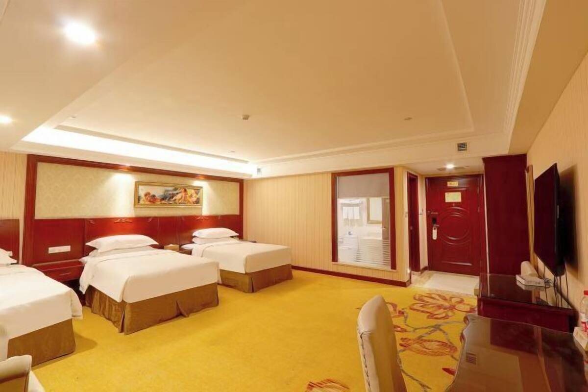 A hotel room with two beds, a desk, a chair, a television, and a painting on the wall.