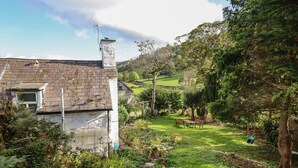Ein Haus mit Steinziegeldeckung und Schornstein, umgeben von einem üppigen Garten mit Rasenfläche, Bäumen und einer Schaukel.