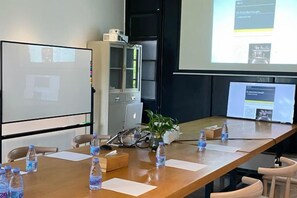 Een vergaderruimte met een lange tafel, stoelen, een projectiescherm en een whiteboard.
