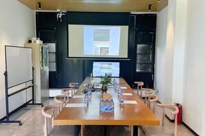 Un salón de conferencias con una larga mesa, sillas, una pantalla de proyector y una pizarra.