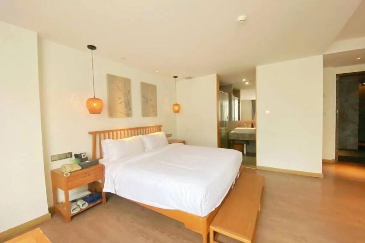 Een slaapkamer met een houten bed, nachtkastje en een bankje. In de achtergrond is een badkamer zichtbaar.