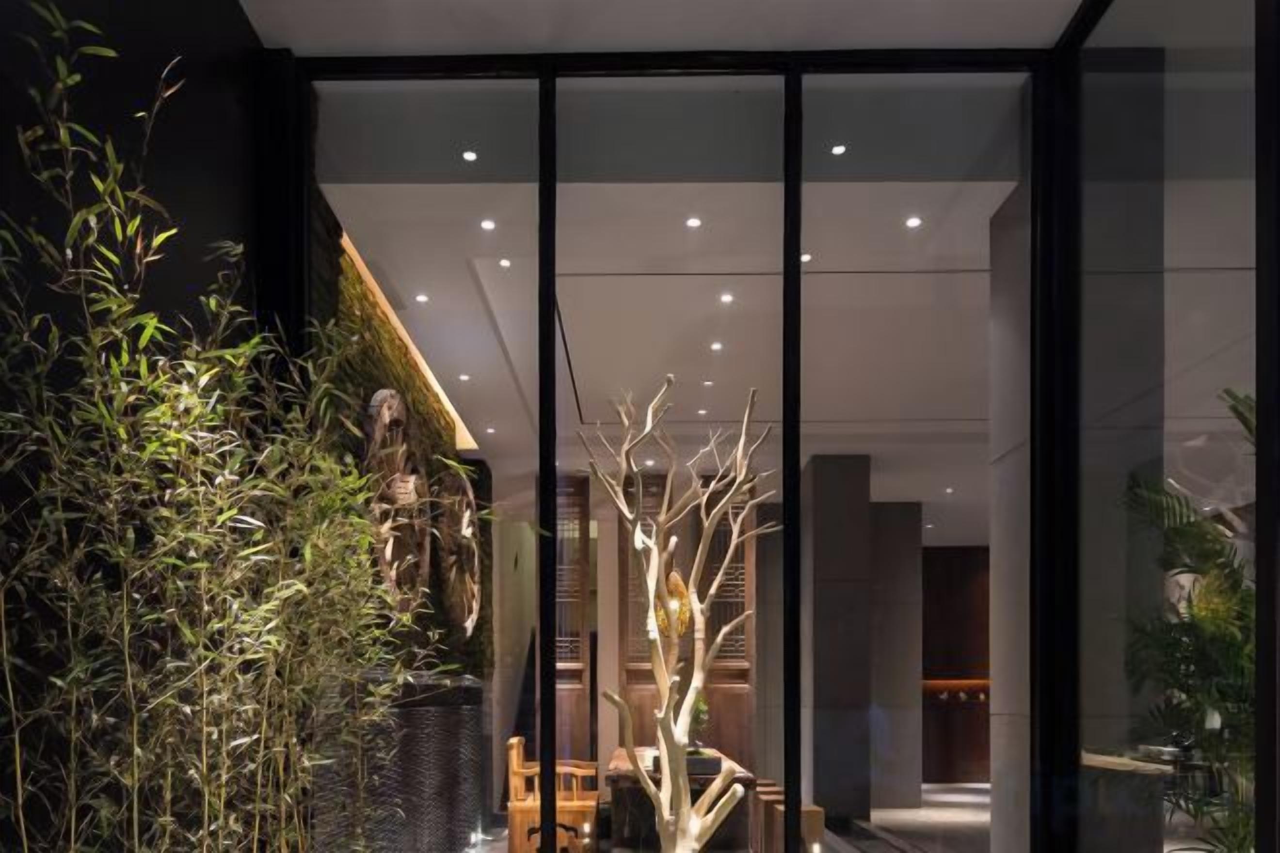 Een modern interieur met een glazen scheidingswand, kamerplanten en een trap naar een hoger niveau.