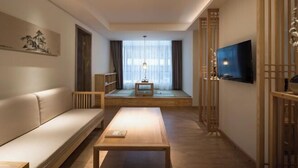 Ein modernes Wohnzimmer mit einer Couch, einem Couchtisch, einem Fernseher und einem Fenster mit Vorhängen.