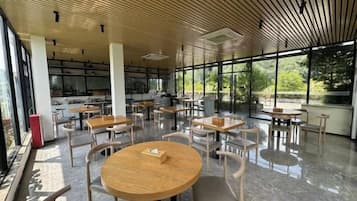 A modern indoor space with round tables and chairs, large windows, and a wooden ceiling.