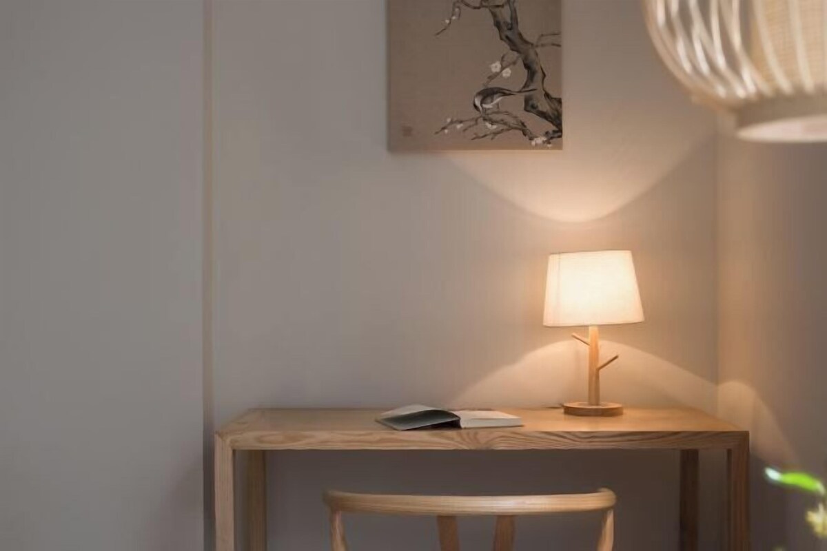 Una pequeña mesa de madera con una lámpara, una silla y un libro encima.