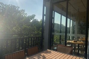 Een balkon met houten vloer en stoelen, met uitzicht op een bebost gebied.