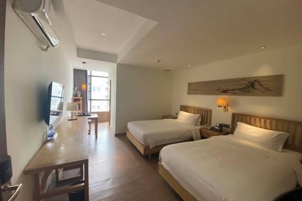 Een hotelkamer met twee bedden, een bureau, een televisie en een schilderij aan de muur.