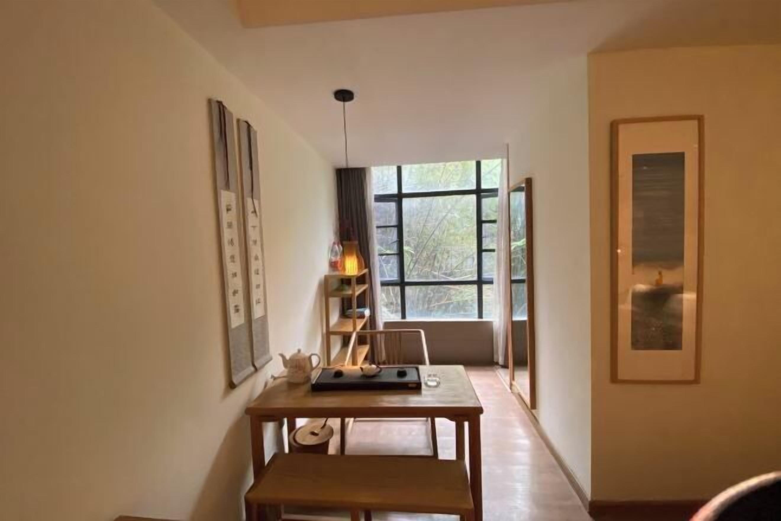 A room with a wooden table, a bench, a window with a view of trees, and a framed picture on the wall.