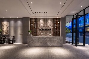 Un área de recepción con mostrador de mármol, estanterías con libros y vistas a través de puertas de vidrio.