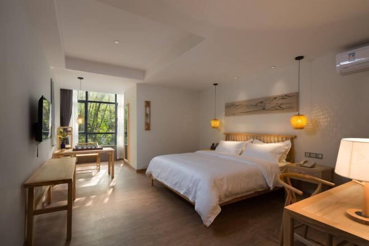 Een moderne slaapkamer met een groot bed, houten meubels en uitzicht op groen.