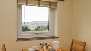 Una pequeña mesa de comedor con vistas a colinas ondulantes, una tetera blanca, dos tazas y un plato de scones.