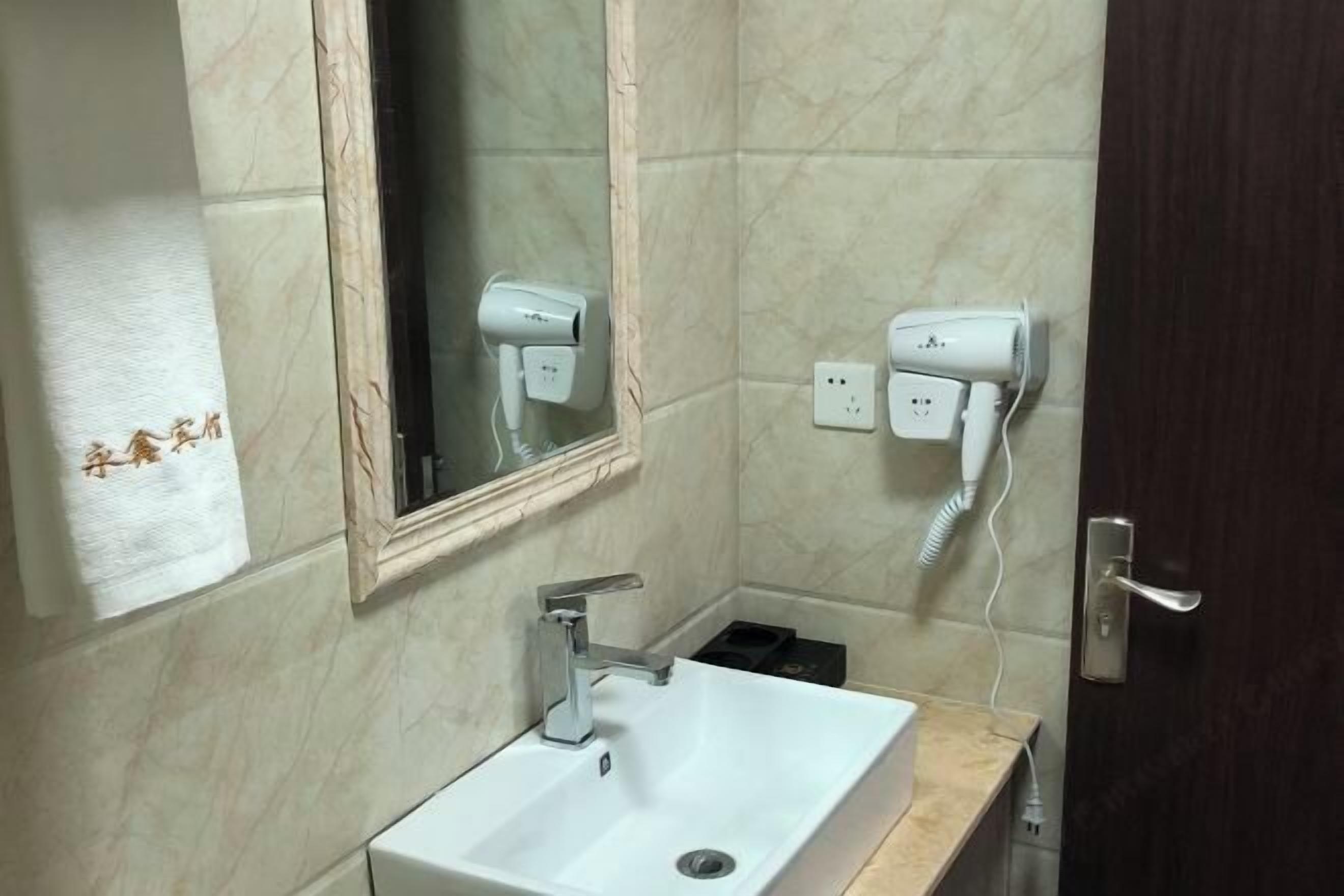 A bathroom with a white sink, a mirror, and two hair dryers plugged into wall sockets.