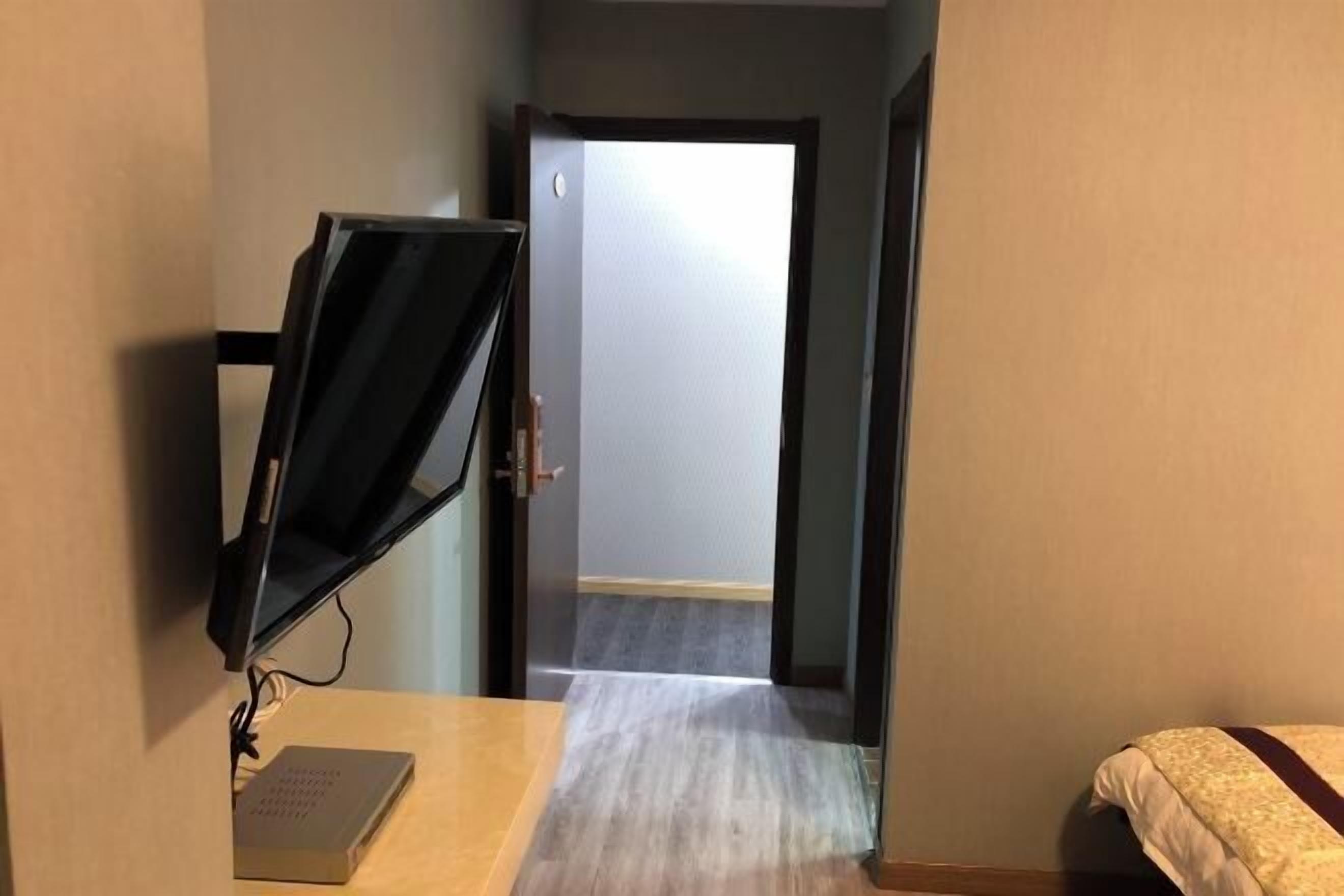 A hotel room with a desk, a computer monitor, a bed, and a door leading to another room.
