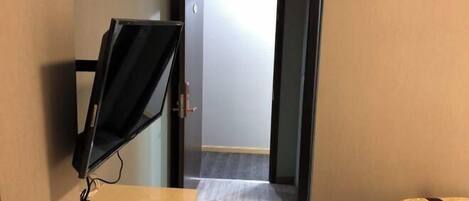 A hotel room with a desk, a computer monitor, a bed, and a door leading to another room.