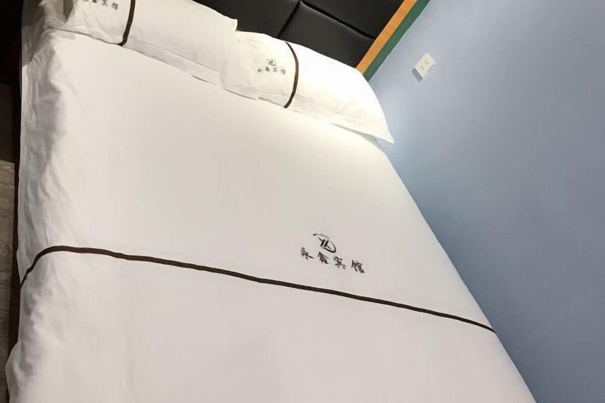 A neatly made bed with a white bedspread and pillows, and a logo on the bedspread.