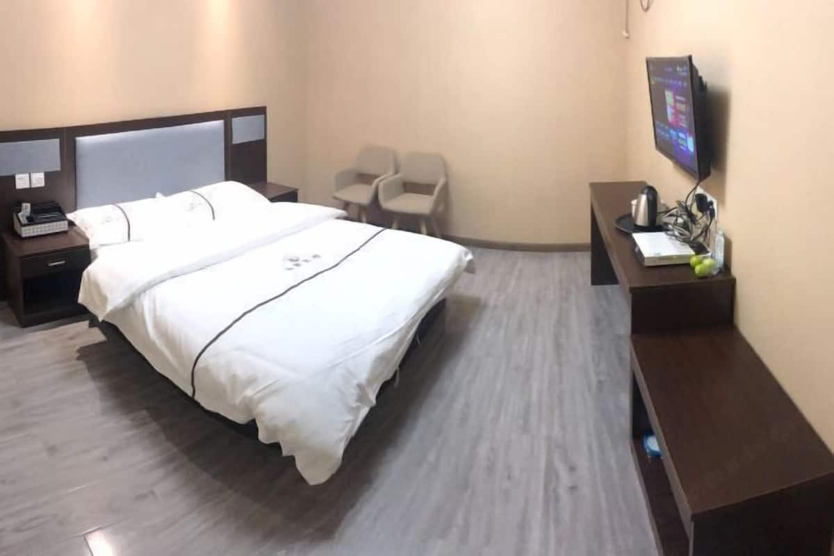 A hotel room with a bed, a desk with a computer, a chair, and a TV on the wall.