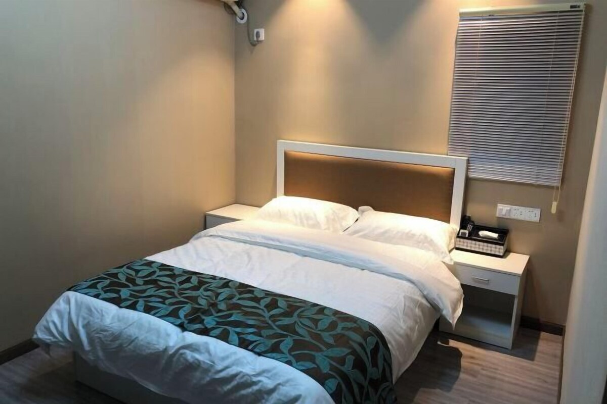 A hotel room with a bed, bedside tables, a nightstand, a lamp, and a window with blinds.