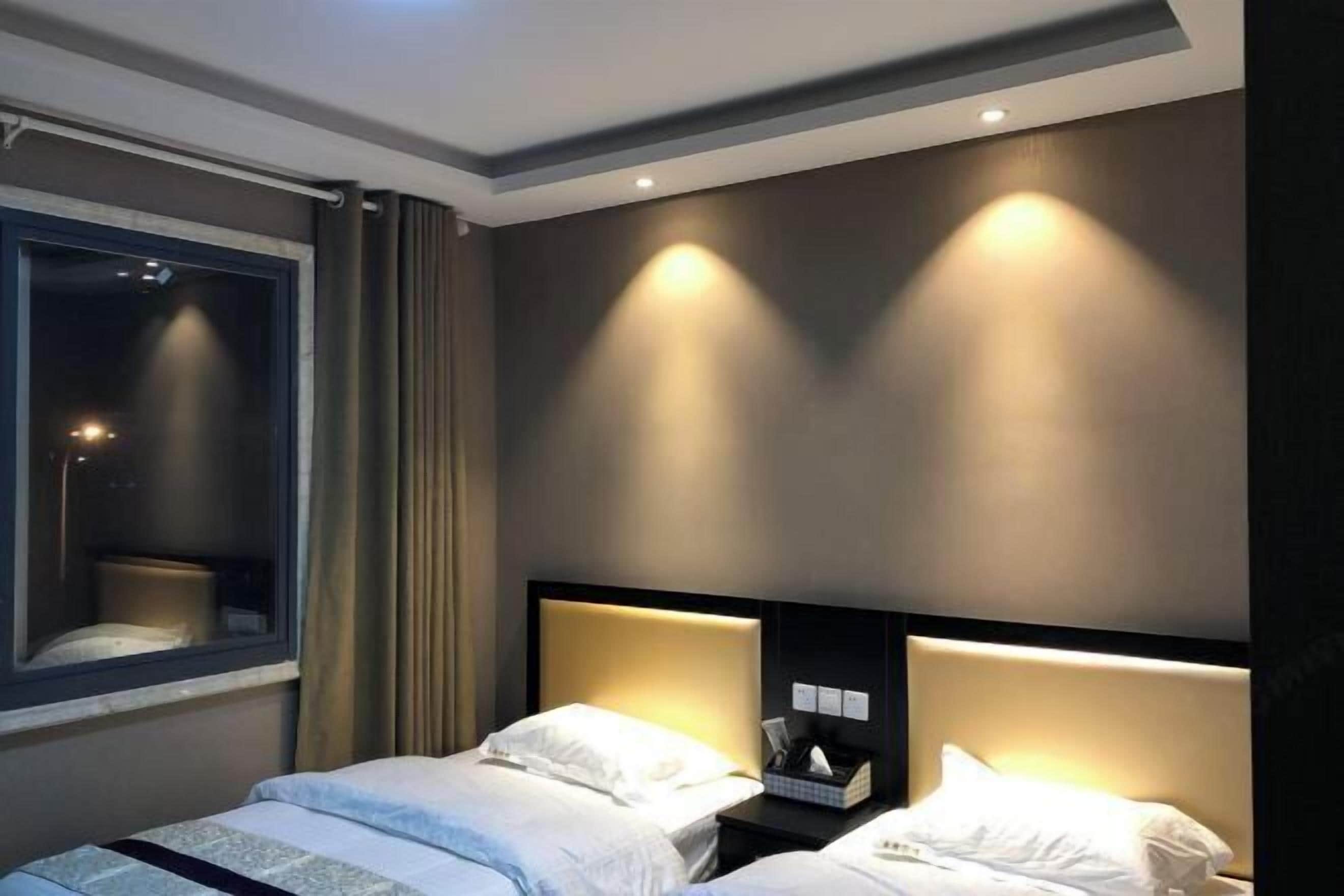 Habitación de hotel con dos camas, un ventanal con cortinas e iluminación en la pared.
