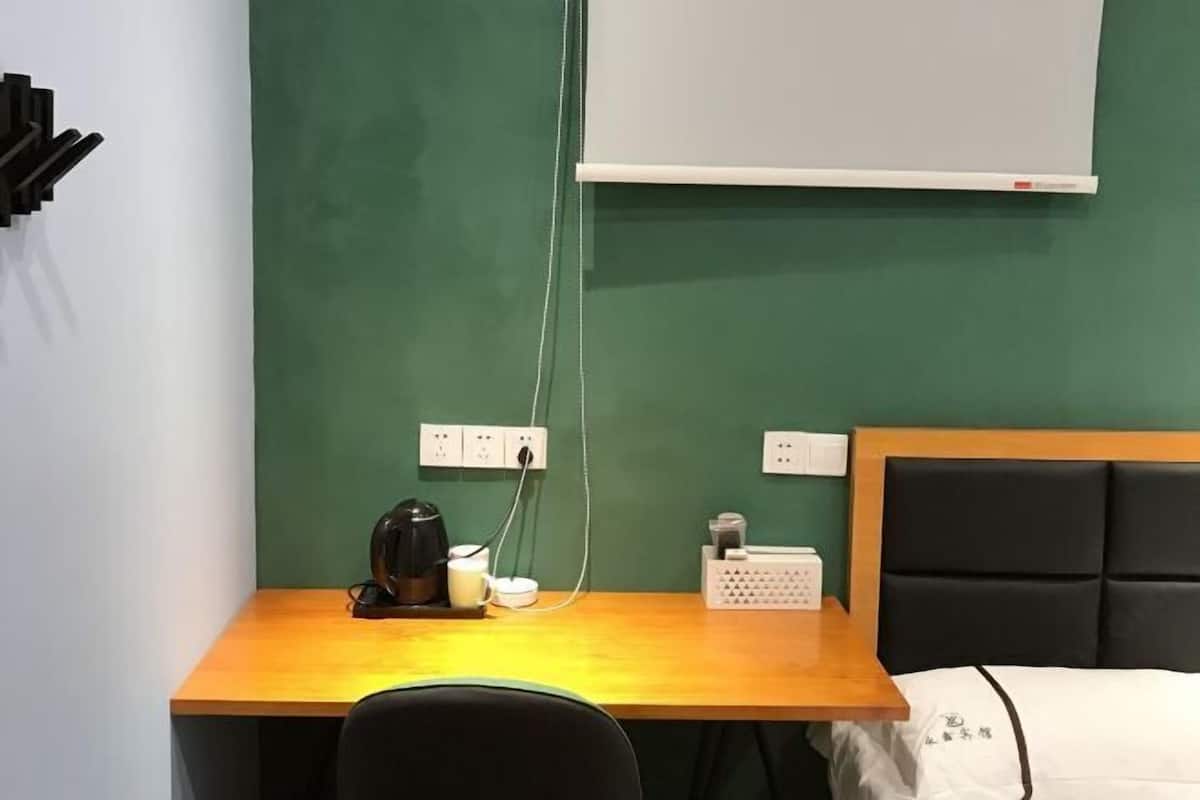 A hotel room with a wooden desk, a black chair, a bed with a black headboard, and a white wall with a whiteboard.