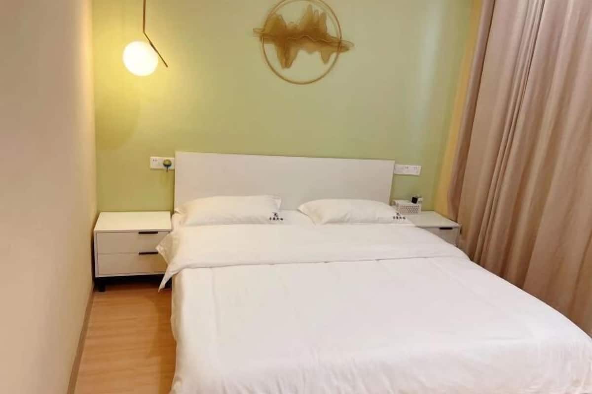 A neatly made bed with white bedding, a bedside table with a lamp, and a wall-mounted artwork.