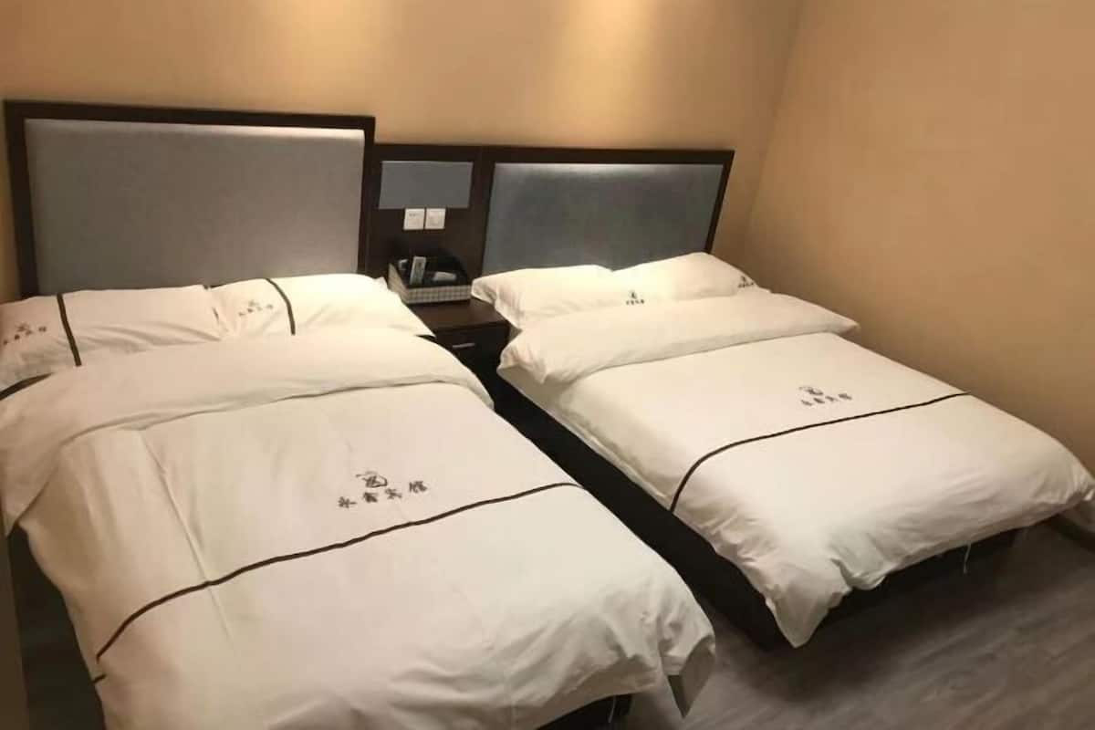 A hotel room with two beds, each with white bedding and a small table between them.