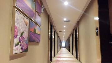 A hotel corridor with artwork on the walls, a long hallway, and doors on the right.