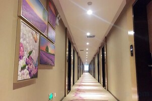 A hotel corridor with artwork on the walls, a long hallway, and doors on the right.