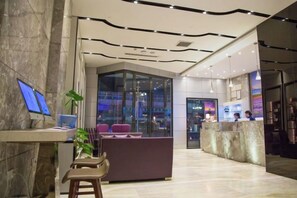 Un moderno vestíbulo de hotel con mostrador de recepción, zona de estar y un separador de vidrio.