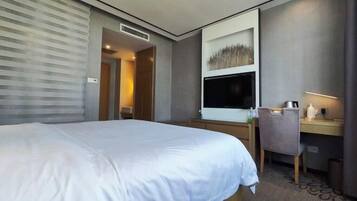 A hotel room with a large bed, a desk with a computer, a TV, and a chair.