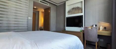A hotel room with a large bed, a desk with a computer, a TV, and a chair.