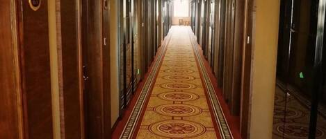 A hotel hallway with a carpeted floor, doors on both sides, and a bright light at the end.