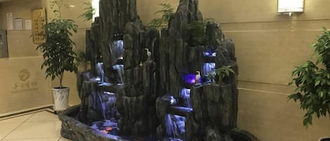Una fuente decorativa con diseño rocoso, rodeada de plantas en macetas.