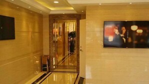 A hotel lobby with a polished floor, a large flat-screen TV on the wall, and a glass elevator. - East Guesthouse (Muling)
