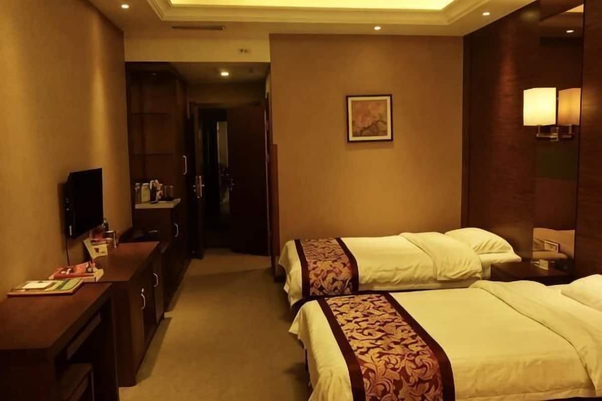 Una habitación de hotel con dos camas, un escritorio con televisor y un espejo.