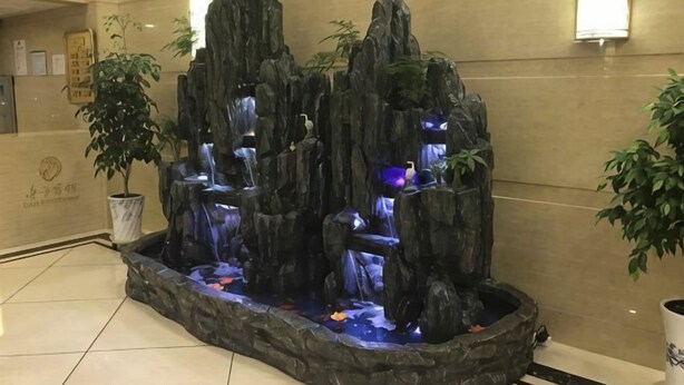 A rock waterfall feature with a potted plant to the left. - East Guesthouse (Muling)