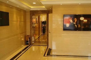 Un pasillo de hotel con piso pulido, una puerta que da a otra habitación y una pantalla de televisión en la pared.