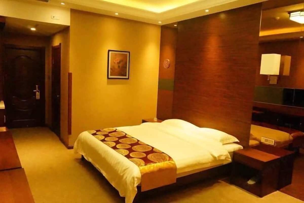 Una habitación de hotel con cama, mesita de noche, espejo y televisor montado en la pared.